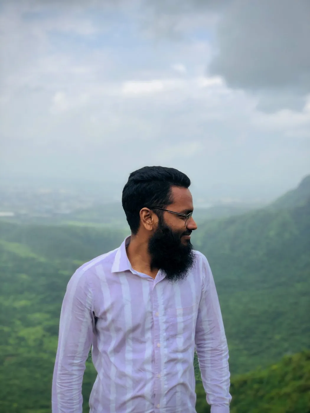 Arif Ansari standing on a hilltop above misty green valleys